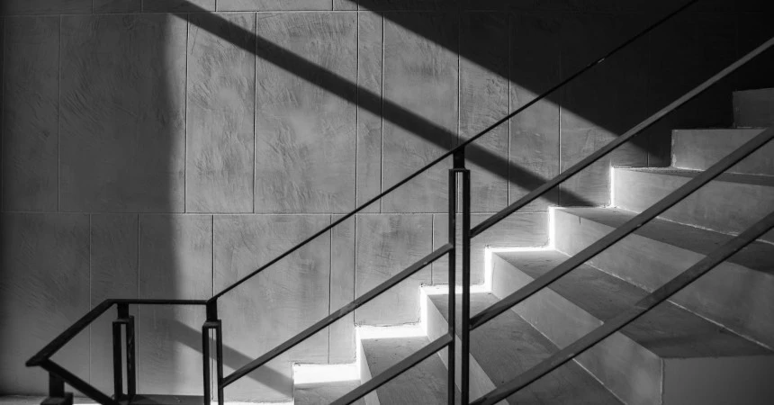 A stairwell with concrete stairs with iron rail and some sunshine shining in.